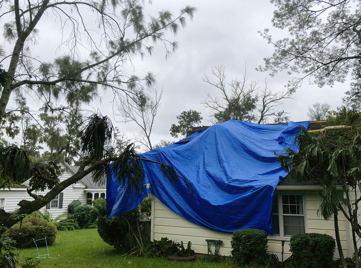 Emergency roof tarping operation on a South Alabama residential home after hurricane damage with a roofing crew securing heavy-duty reinforced polyethylene tarp from ridge to eave using mechanical fasteners and wood battens, the critical first emergency response that stops interior water damage within 24 to 48 hours after a Gulf Coast storm event in Mobile County where exposed decking and displaced shingles leave homes vulnerable to continued rain infiltration